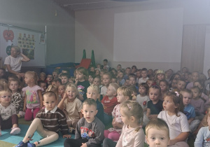 Dzieci siedzą na dywanie oglądając przedstawienie
