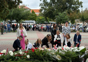 Dzieci razem z nauczycielami składają kwiaty pod pomnikiem