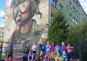 dzieci z grupy "Wiewiórek" stoja na scenie przed muralem dywizjonu