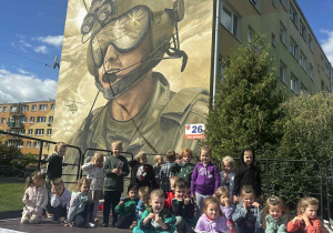grupa "Biedronki" dzieci stoi na scenie przed muralem dywizjonu