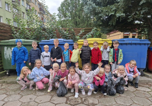 Dzieci z grupy "Sowy" stoją z workami przed pojemnikami na śmieci