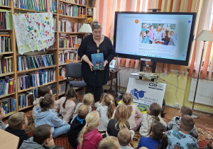 Dzieci siedzą na dywanie i słuchają bajki.