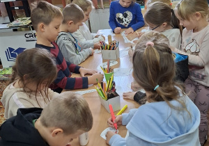 Dzieci przy stolikach kolorują obrazki z kwiatkami.