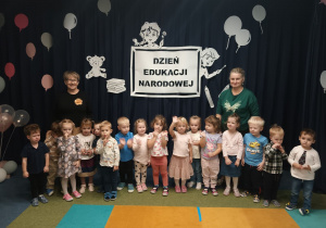 Dzieci w grupie stoją z wychowawcą na tle dekoracji