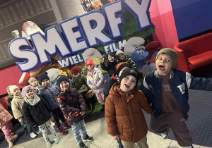 Dzieci pozują do zdjęcia, w tle reklama filmu Smerfy