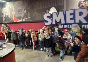 Dzieci pozują do zdjęcia, w tle reklama filmu Smerfy