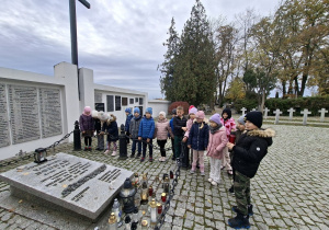 Dzieci stoją wokół tablicy pamiątkowej żołnierzy poległych w czasie II wojny światowej