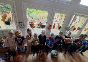 Dzieci stoją na korytarzu w otoczeniu swoich przygotowanych na konkurs dyń