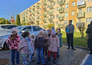 Dzieci z grupy "Sowy" stoją przed bramą przedszkola wraz z opiekunem