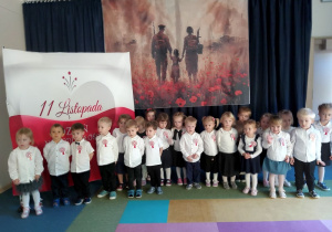 Dzieci z grupy "Kotki" stoją na tle symboli narodowych