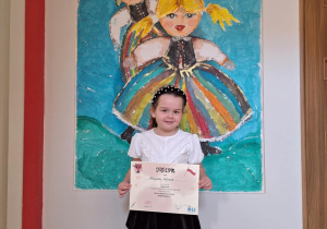 Dziewczynka stoi z dyplomem na tle pyzy wędrowniczki