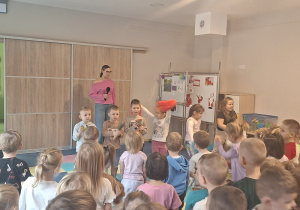 Kilkoro dzieci razem z prowadzącymi tańczy i gra do muzyki