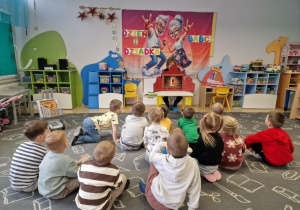 Dzieci siedzą na dywanie i oglądają teatrzyk