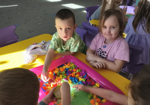 Dzieci przy stoliku szukają figurki dinozaurów w piasku