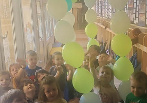 Grupa dzieci stoi pod postacią dinozaura z balonów