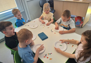 Dzieci przy stoliku układają sylwety warzyw na talerzykach