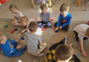 Dzieci siedzą z woreczkami na dywanie