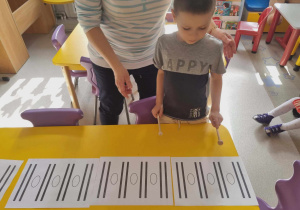 Chłopiec stoi z pałeczkami przed obrazkami z rytmami