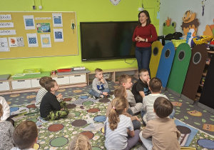 Dzieci siedzą na dywanie słuchając prowadzącej