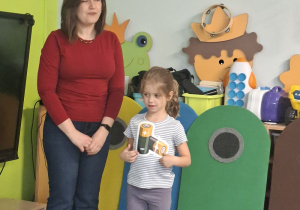 Prowadząca stoi obok diewczynki z sylwetą baterii