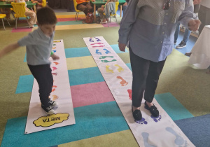 Dzieci razem z dzadkami chodzą po macie edukacyjnej