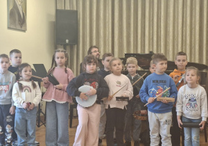 Grupa dzieci na scenie trzymają w rękach rózne instrumenty