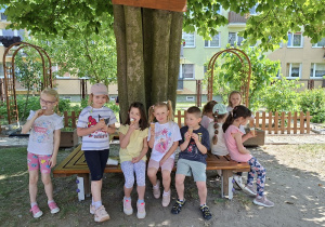Grupa dzieci je lody pod drzewem