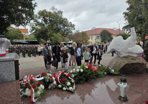 Dzieci wraz z nauczycielami podchodzą pod pomnik z kwiatami w ręku
